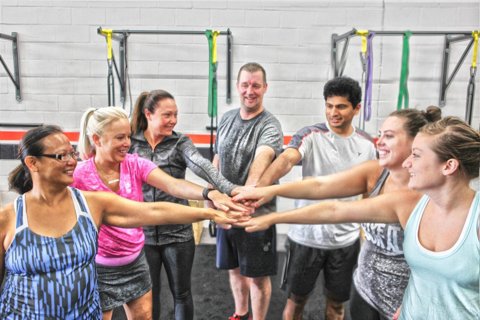 Altman Fitness members and coaches stacking hands in a huddle after class